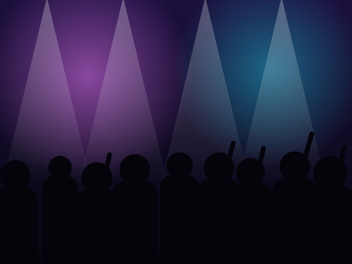 A crowd with hands in the air in front of coloured stage lights